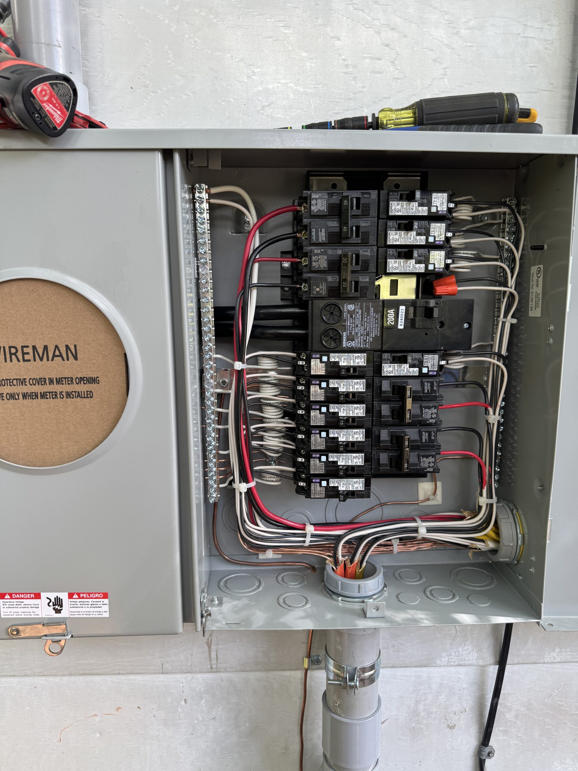 An open electrical breaker panel with visible circuit breakers, wiring, and tools resting on top of the panel.